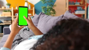 Person holding a smartphone with a green screen.