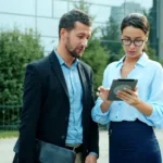 Two colleagues discussing a tablet outside office building