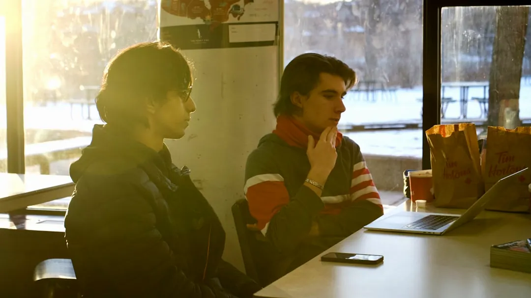 two people sitting at a table in front of a laptop computer