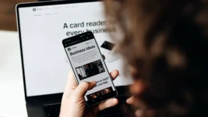 A person holding a cell phone in front of a laptop