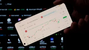 A person holding a cell phone in front of a laptop