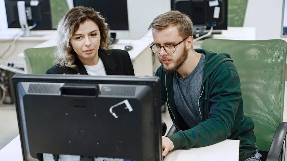 Two colleagues working together on a computer in an office, focusing on a shared task.