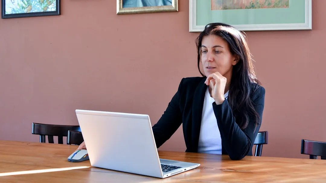 Woman in a black blazer working on a laptop.