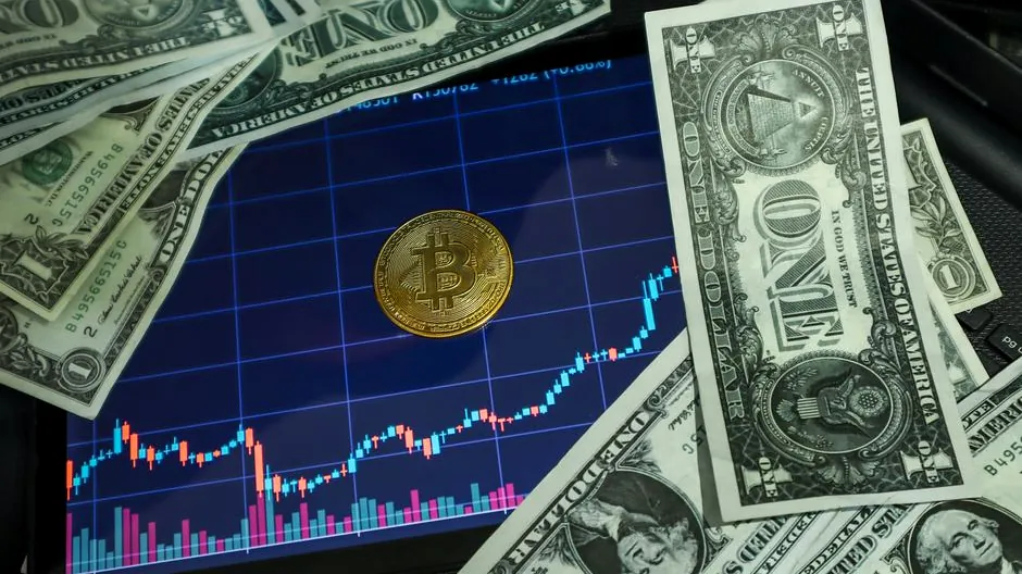 Bitcoin coin on a tablet showing stock chart, surrounded by dollar bills.