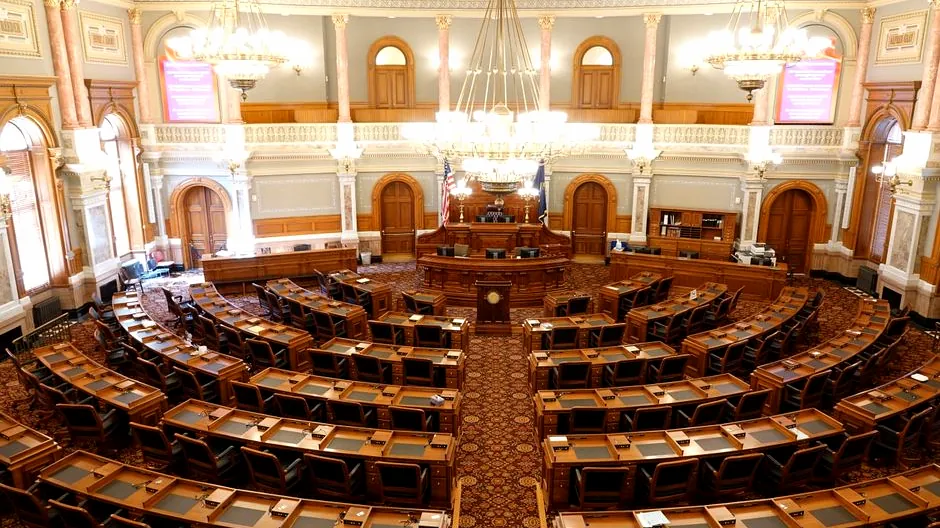 Wide view of an ornate legislative chamber with empty seats and chandeliers.